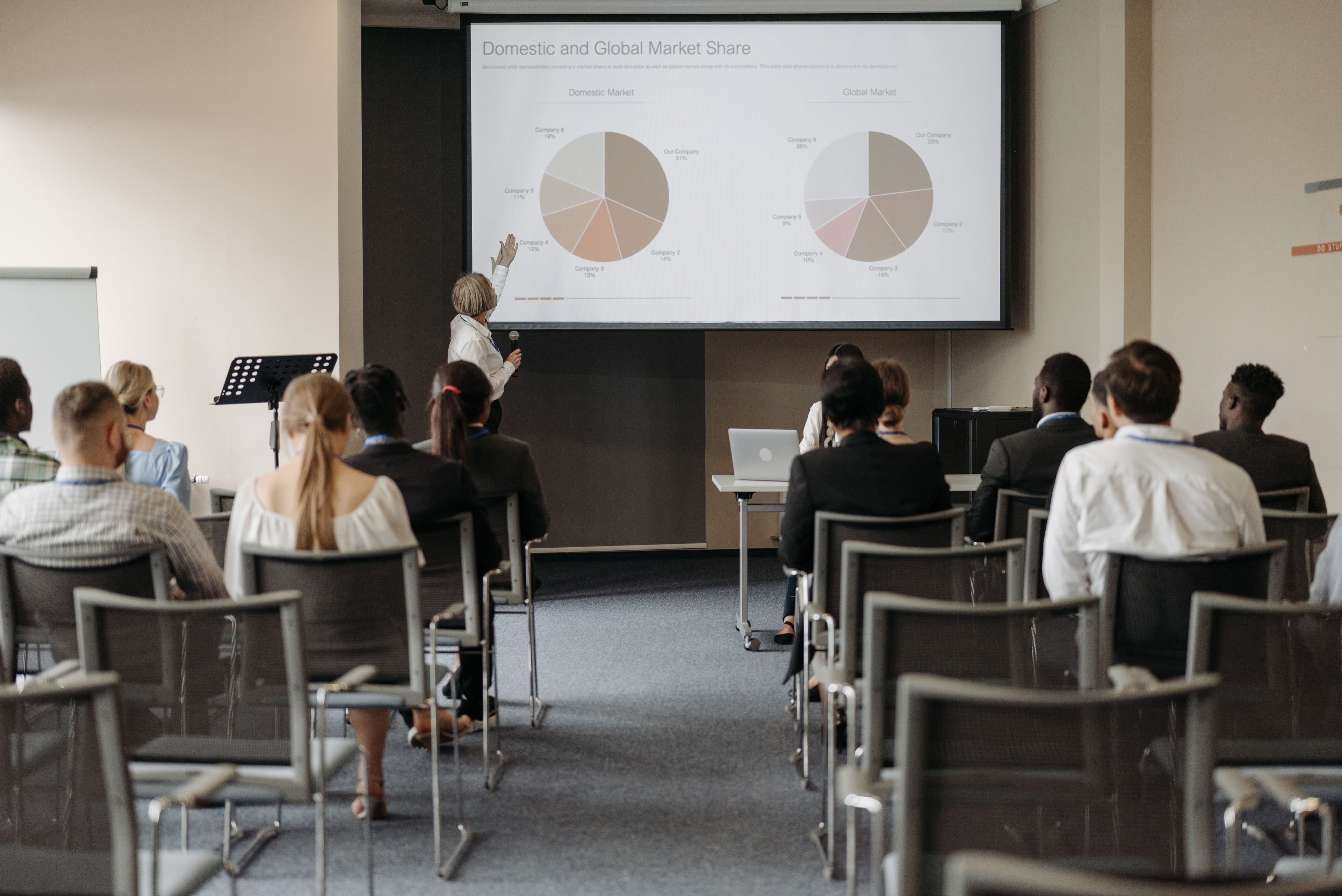 Præsentation af markedsandele med cirkeldiagrammer på projektionsskærm foran publikum i mødelokale